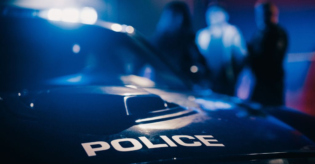 hood of a police car with police officers arresting a suspect in the background